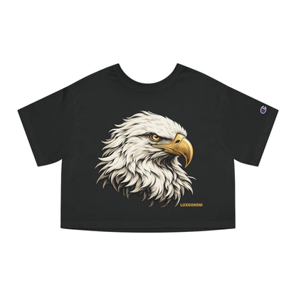 A black short-sleeve crop top t-shirt featuring a detailed graphic of a bald eagle's head on the front, with a small Champion logo on the left sleeve and 'LUXGONSNI' printed in gold near the bottom hem.